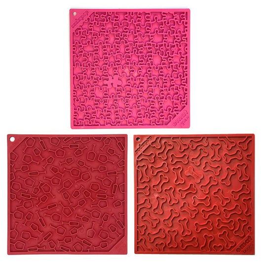 Three square licking mats in pink, and red,  each featuring a unique embossed pattern, arranged on a plain white background.